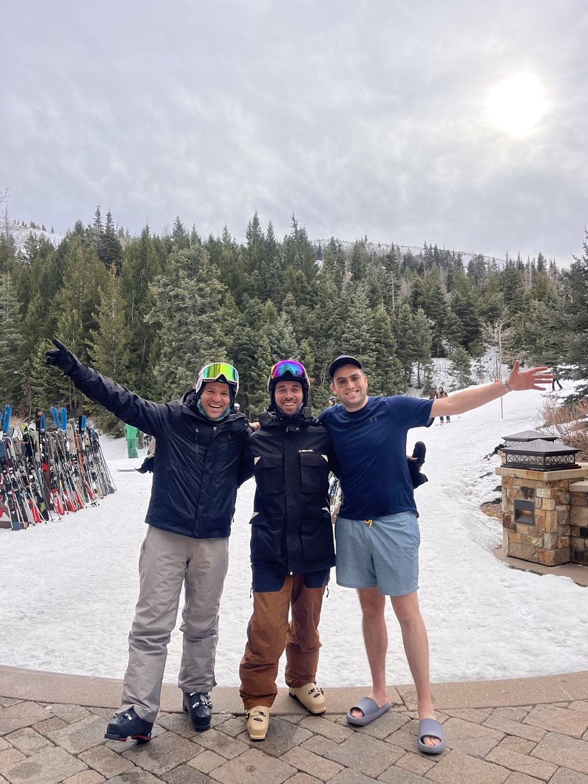 Tres amigos saludando al sol en la base de una montaña de ski